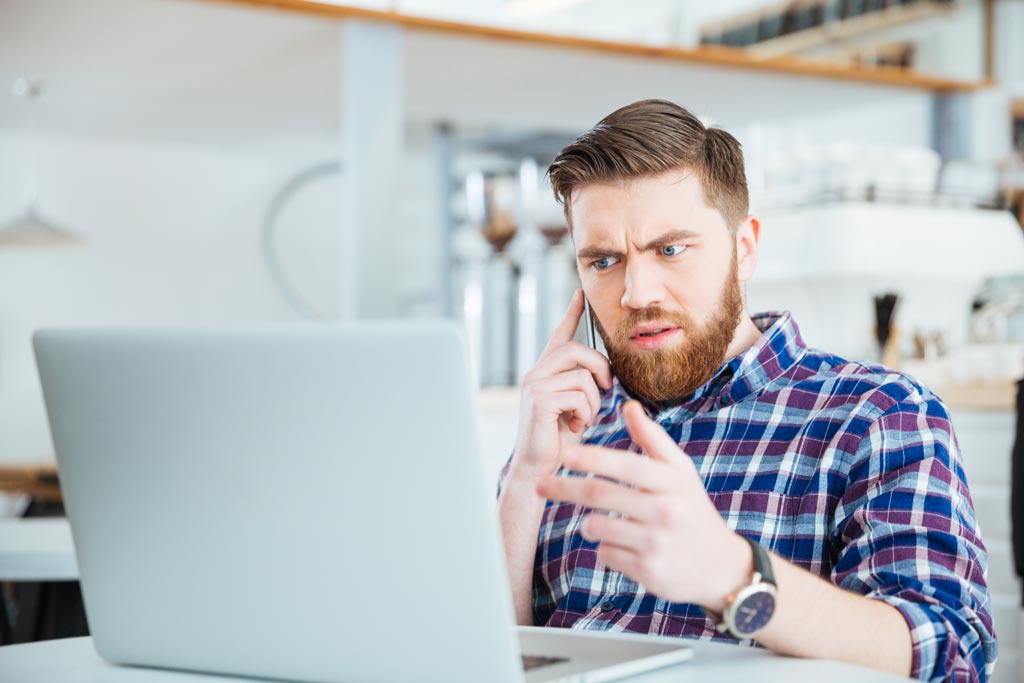 Mann sitzt vorm Laptop und telefoniert