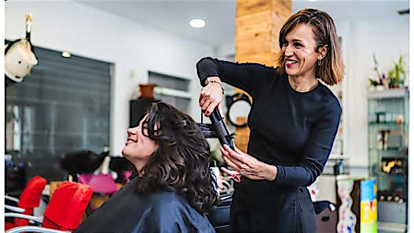 Kassensystem Friseure Friseurin wellt Kundin Haare mit Lockenstab